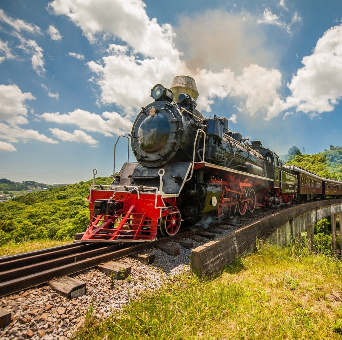 Imagem de um trem á vapor preto e vermelho andando pelas trilhos perto do campo. Na parte superior da imagem, tem o texto: 'Bento Gonçalves Rio Grande do Sul'